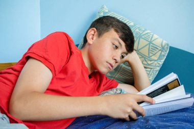 Beyaz genç çocuk başını destekleyen bir yatağa atma bir kitap okuma