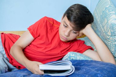 Beyaz genç çocuk başını destekleyen bir yatağa atma bir kitap okuma