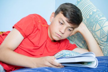 Beyaz genç çocuk başını destekleyen bir yatağa atma bir kitap okuma