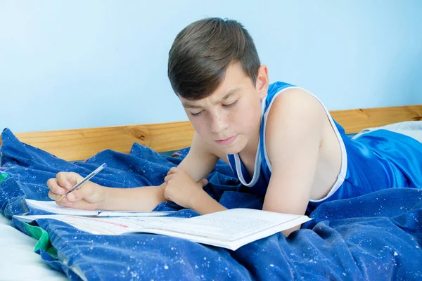 Bir ders kitabı okuma onun yatağında döşeme beyaz genç çocuk