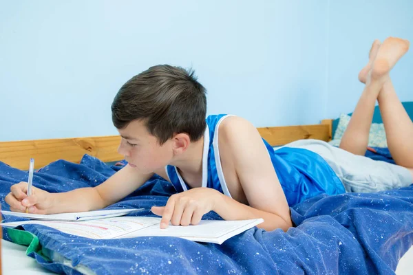 十代の少年が彼のベッドの上の宿題 — ストック写真