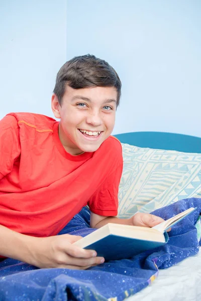 笑いながらベッドの上に敷設本を読んで 代の白人の少年 — ストック写真