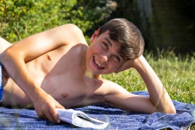 Genç çocuk bir bahçe gülümseyen güneş banyosu sırasında bir kitap okuma