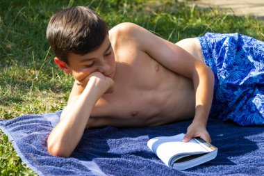Genç çocuk bir bahçede güneşlenme sırasında bir kitap okuma