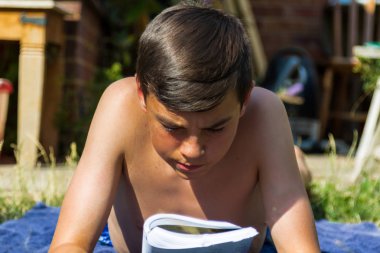 Genç çocuk bir bahçede güneşlenme sırasında bir kitap okuma