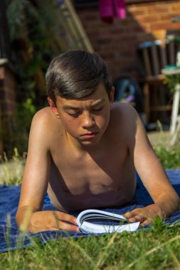 Genç çocuk bir bahçede güneşlenme sırasında bir kitap okuma