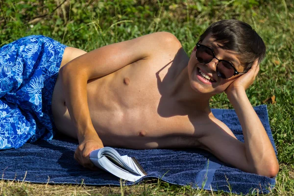 Nastoletni Chłopak Czytanie Książki Opalając Się Ogrodzie Noszący Okulary Przeciwsłoneczne — Zdjęcie stockowe