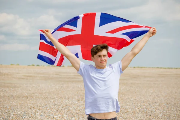 Kaukasisk hane på en strand som håller en brittisk flagga — Stockfoto