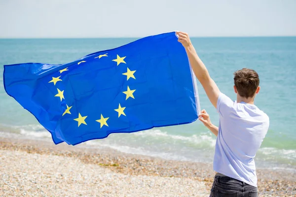 Kaukasiska hane på en strand som innehar en EU-flagga — Stockfoto