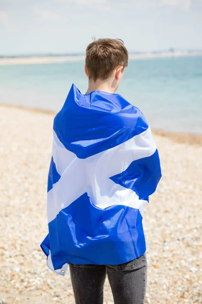 Kaukasisk hane på en strand som håller en skotsk flagga — Stockfoto