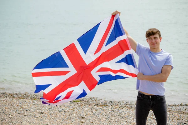 Kaukasisk hane på en strand som håller en brittisk flagga — Stockfoto