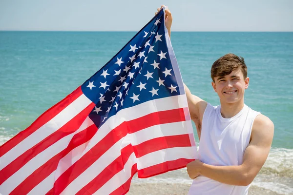 Homem caucasiano em uma praia segurando uma bandeira americana — Fotografia de Stock