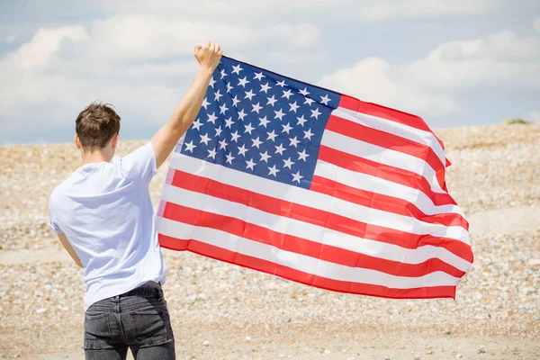 Caucasian male on a beach holding an American flag — Stock Photo, Image