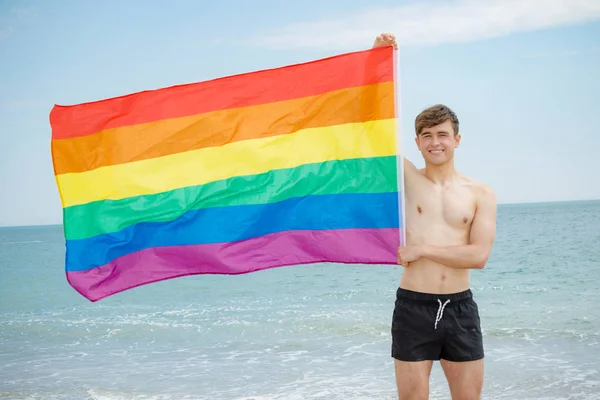 Caucasian male on a beach holding a Pride flag — Stock Photo, Image