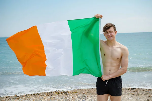 Homem caucasiano em uma praia segurando uma bandeira irlandesa — Fotografia de Stock