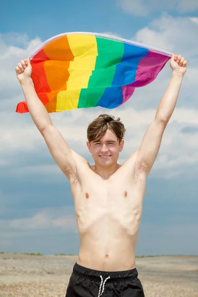 Homem caucasiano em uma praia segurando uma bandeira do orgulho — Fotografia de Stock