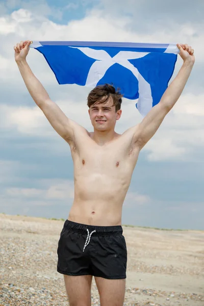 Kaukasisk hane på en strand som håller en skotsk flagga — Stockfoto