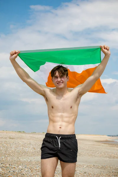 Homem caucasiano em uma praia segurando uma bandeira irlandesa — Fotografia de Stock