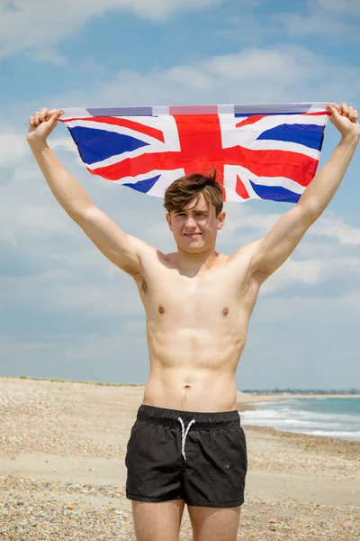 Homem caucasiano em uma praia segurando uma bandeira britânica — Fotografia de Stock