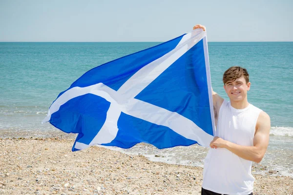 Kaukasisk hane på en strand som håller en skotsk flagga — Stockfoto