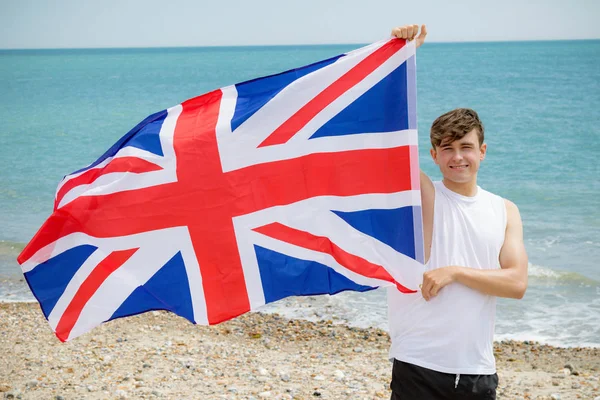 Kaukasisk hane på en strand som håller en brittisk flagga — Stockfoto