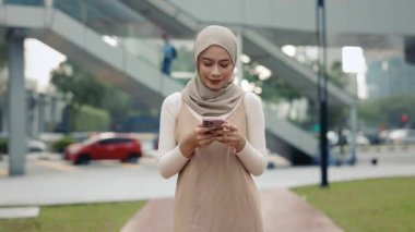 Başörtüsü takan kadın portresi şehir parkında akıllı telefon yürüyüşleriyle yön buluyor. Mutlu Malezyalı bayan ofis çalışanı sokakta cep telefonuyla iş sohbetini okuyor. Şehir hayatı