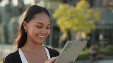 Kendine güvenen Asyalı kadın portresi şirket binasının yakınındaki dijital tablet ekranına dokunuyor. Esmer kadın yönetici şehir merkezindeki taşınabilir bilgisayardaki verileri kontrol ediyor.