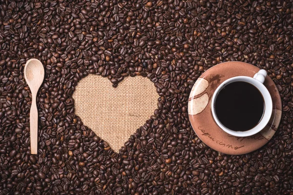 Herzförmige Kaffeebohnen Auf Juta Textil Mit Holz Teelöffel Und Cappuccino — Stockfoto