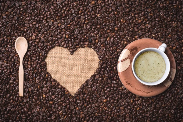 Herzförmige Kaffeebohnen Auf Juta Textil Mit Holz Teelöffel Und Cappuccino — Stockfoto