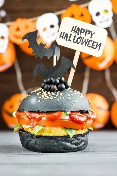 Halloween Spooky Black Burger with Cheese. Cheeseburger on Halloween pumpkin head jack lantern background