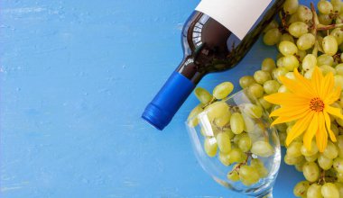 Taze beyaz üzümler ve mavi ahşap bir doku yüzeyinde bir şişe şarap ve cam. Reklam metni için alan