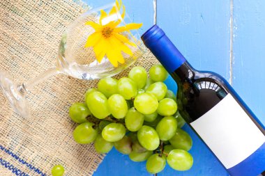 Taze beyaz üzümler ve mavi ahşap bir doku yüzeyinde bir şişe şarap ve cam. Reklam metni için alan