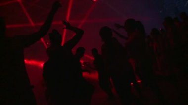 Tekno parti. İnsanlar dans eder, DJ çalar. Her yerde renkli ışıklar