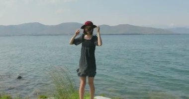 Kız rıhtımda takılıyor, sahilde yürüyor. Kameranın önünde poz vermek, gülümsemek, kumda yalın ayak yürümek, rüzgarın şalla oynaması.