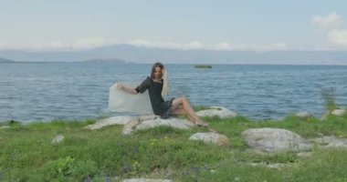 Kız rıhtımda takılıyor, sahilde yürüyor. Kameranın önünde poz vermek, gülümsemek, kumda yalın ayak yürümek, rüzgarın şalla oynaması.