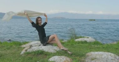 Kız rıhtımda takılıyor, sahilde yürüyor. Kameranın önünde poz vermek, gülümsemek, kumda yalın ayak yürümek, rüzgarın şalla oynaması.