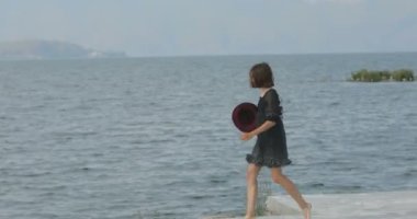 Kız rıhtımda takılıyor, sahilde yürüyor. Kameranın önünde poz vermek, gülümsemek, kumda yalın ayak yürümek, rüzgarın şalla oynaması.