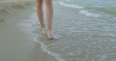 Kumsalda yürüyen bir kız. Kameranın önünde poz vermek. Gülümsüyor, kumda yalın ayak yürüyor, rüzgar şalla çalınıyor.