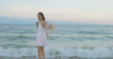 Kumsalda yürüyen bir kız. Kameranın önünde poz vermek. Gülümsüyor, kumda yalın ayak yürüyor, rüzgar şalla çalınıyor.