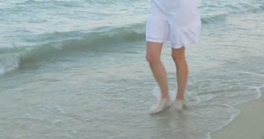 Kumsalda yürüyen bir kız. Kameranın önünde poz vermek. Gülümsüyor, kumda yalın ayak yürüyor, rüzgar şalla çalınıyor.