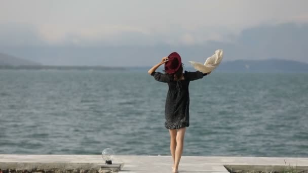 戴帽子的女孩走在码头上 风带着披风嬉戏 动作缓慢 — 图库视频影像