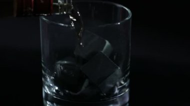 Siyah bir arkaplan önünde viski bir bardak viski taşına dökülür..
