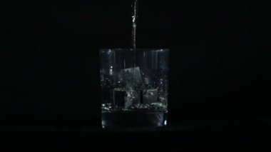 Siyah bir arkaplan önünde viski bir bardak viski taşına dökülür..