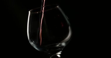 Kırmızı şarabı bir bardağa dolduruyorum, siyah arkaplanın önünde.