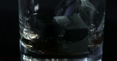 Siyah bir arkaplan önünde viski bir bardak viski taşına dökülür..