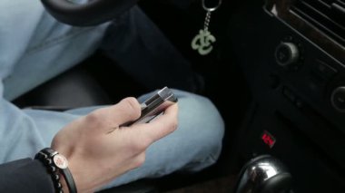Arabasında oturan bir adam cep çakısını açar ve kapatır ve kot pantolonunun cebine koyar.