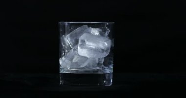 Buzlar alkolde erir, viski bardakları siyah arka planda.