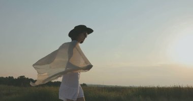 Kumsalda yürüyen bir kız. Kameranın önünde poz vermek. Gülümsüyor, kumda yalın ayak yürüyor, rüzgar şalla çalınıyor.