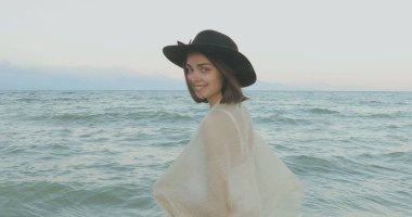 Kumsalda yürüyen bir kız. Kameranın önünde poz vermek. Gülümsüyor, kumda yalın ayak yürüyor, rüzgar şalla çalınıyor.