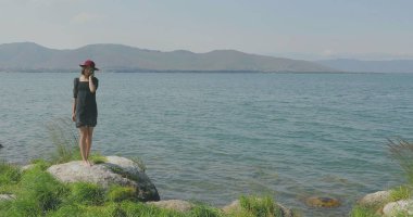 Kız rıhtımda takılıyor, sahilde yürüyor. Kameranın önünde poz vermek, gülümsemek, kumda yalın ayak yürümek, rüzgarın şalla oynaması.